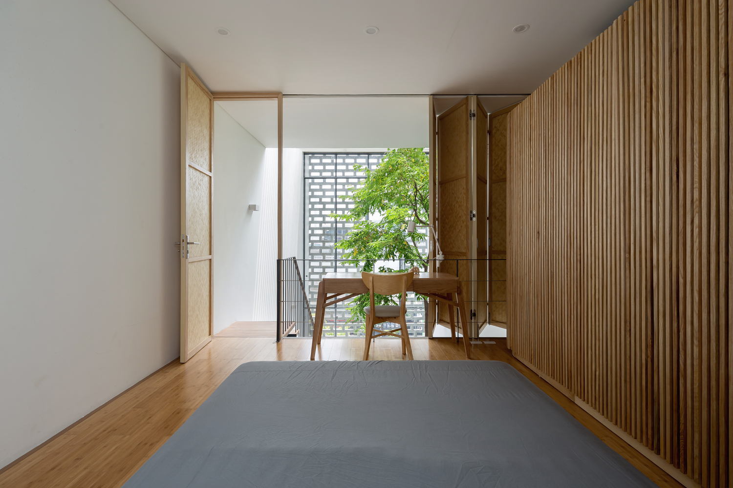 Hình ảnh bên trong một phòng ngủ hiện đại, sử dụng nội thất gỗ đơn giản, bàn ghế nhỏ đặt hướng nhìn ra khoảng thông tầng cầu thang.