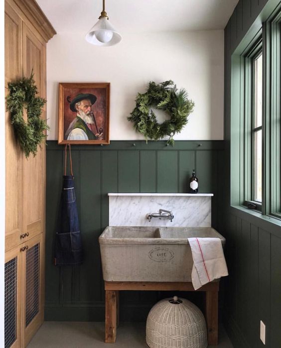 Hình ảnh bên trong một phòng tắm nhỏ với tủ lưu trữ sơn màu xanh lá, tranh trang trí, cây xanh