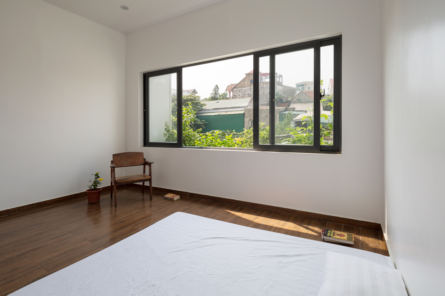 Hình ảnh phòng ngủ với ga gối màu trắng, sàn gỗ, ghế ngồi thư giãn, cửa sổ kính lớn