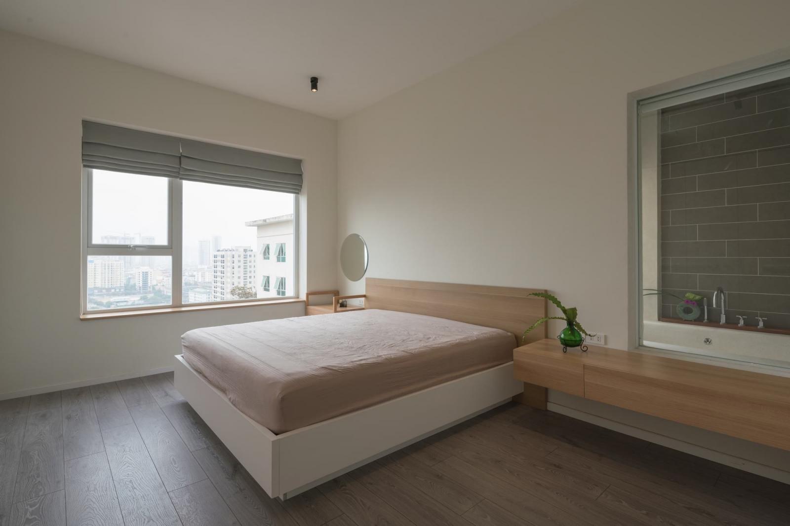 Hình ảnh toàn cảnh phòng ngủ đơn giản với giường lớn, ga màu hồng phấn đặt cạnh cửa sổ kính, hai bên là tab gỗ