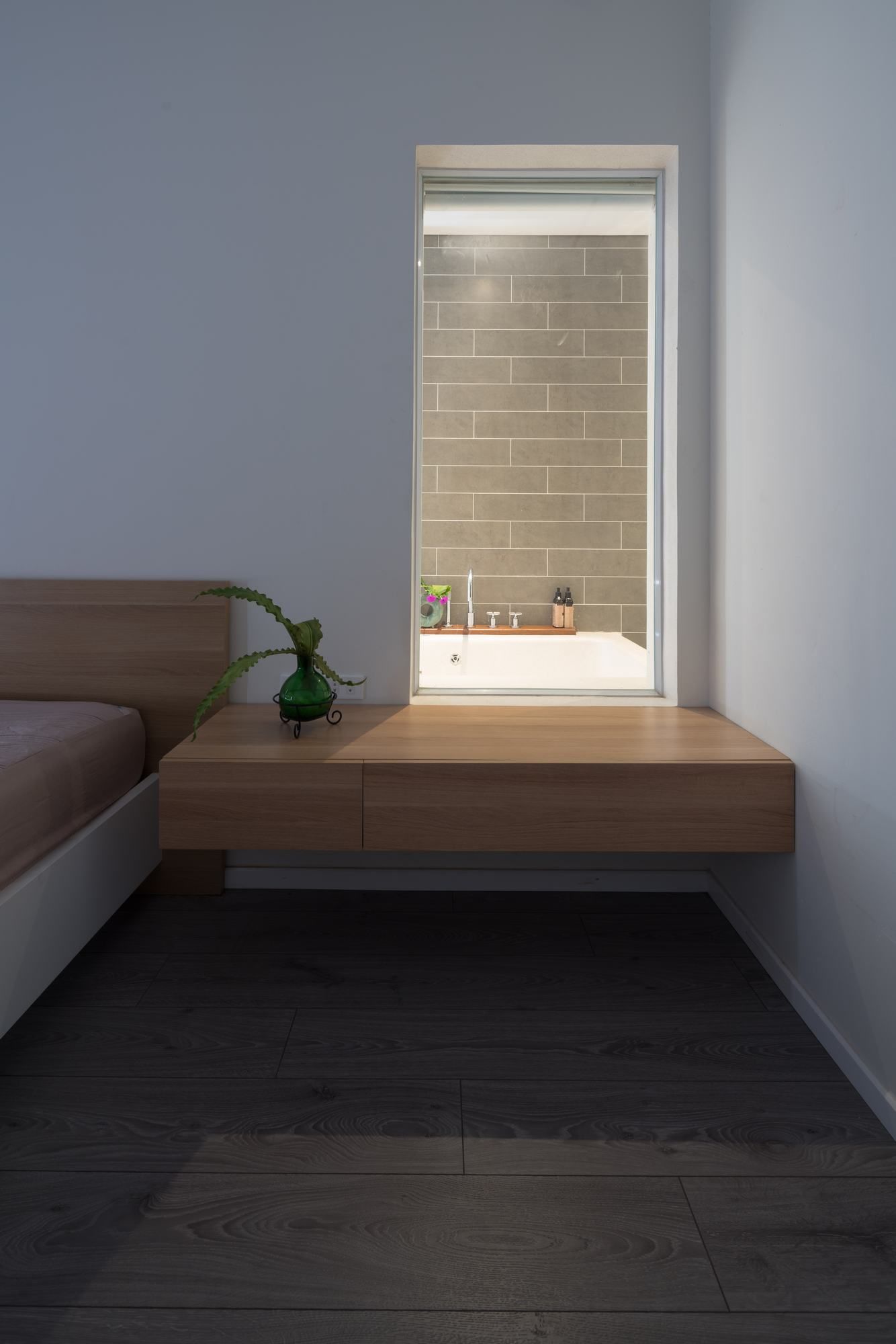 Hình ảnh một góc phòng ngủ với tab gỗ nhỏ cạnh cửa sổ kính nhìn ra phòng tắm