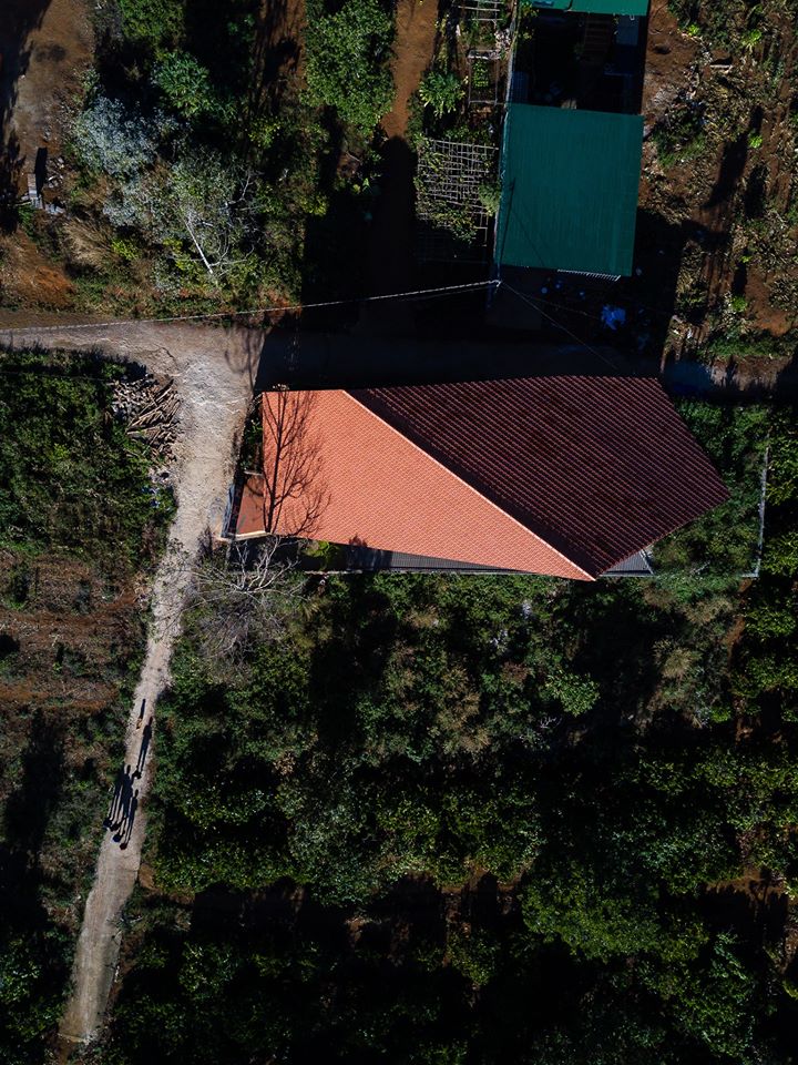 Hình ảnh ngôi nhà chụp từ trên cao với mái ngói đỏ nổi bật, xung quanh là núi rừng xanh ngát