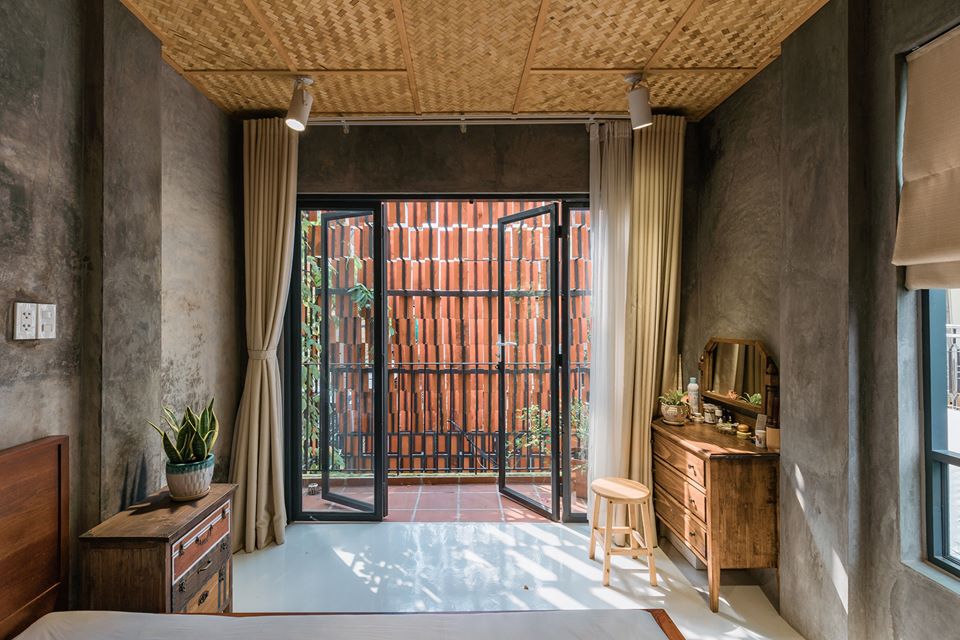 Hình ảnh một căn phòng mộc mạc với tường bê tông không sơn trát, trần ốp phên tre, cửa kính trong suốt mở ra bên ngoài