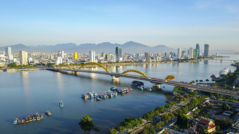 Hình ảnh một góc TP. Đà Nẵng với cầu rồng bắc qua sông, hai bên là các tòa nhà cao tầng xen kẽ khu dân cư thấp tầng