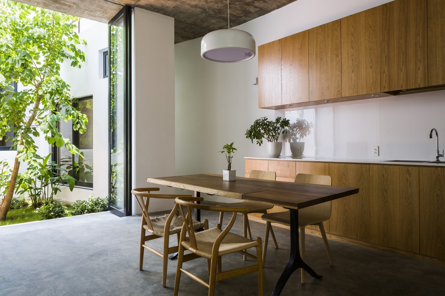 Hình ảnh một góc phòng bếp đơn giản với bàn ăn và tủ bếp bằng gỗ, cửa kính lớn mở ra bên ngoài