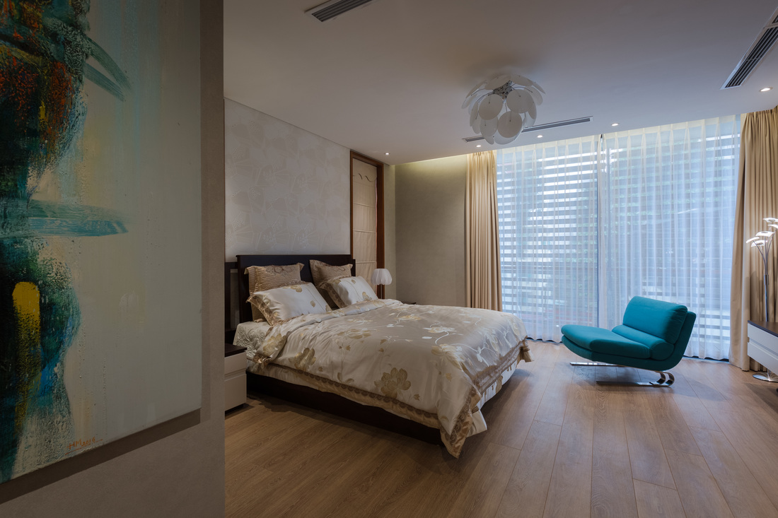Hình ảnh phòng ngủ trong nhà phố rộng rãi với giường nệm cao cấp, ghế ngồi thư giãn màu xanh dương đặt cạnh cửa sổ kính cường lực