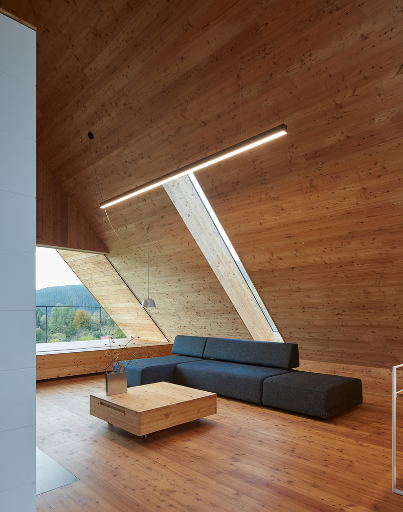 Hình ảnh phòng khách trên tầng áp mái với ghế sofa màu xanh than, bàn trà gỗ, cửa kính lấy sáng