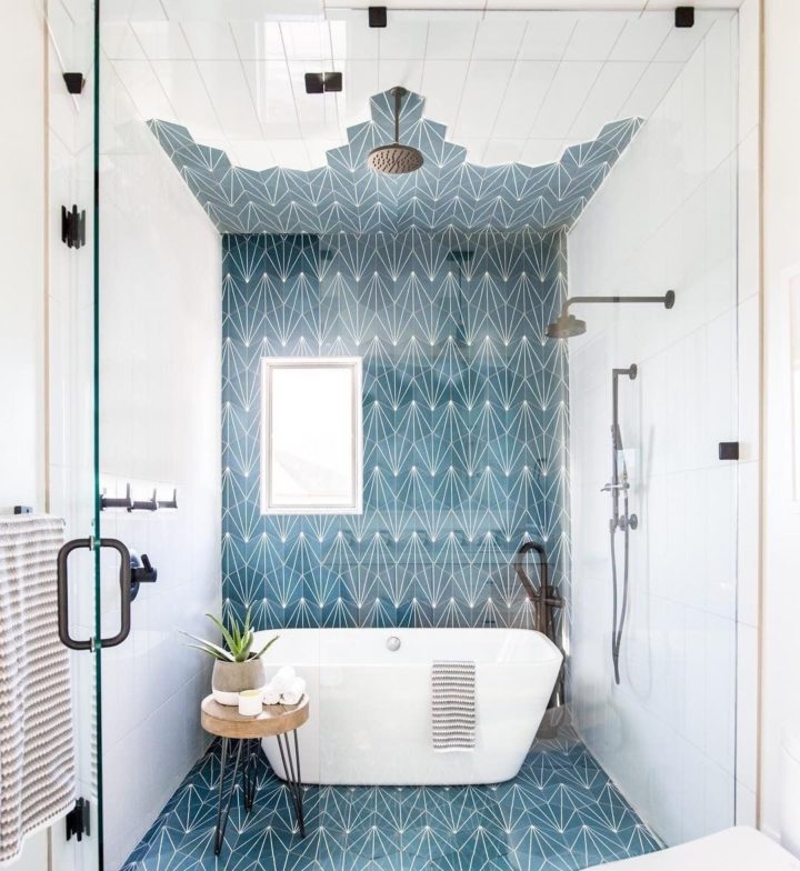 Hình ảnh bên trong phòng tắm hiện đại với chậu cây cảnh nha đam đặt trên bàn gỗ nhỏ, cạnh đó là bồn tắm màu trắng, gạch ốp lát màu xanh dương họa tiết hình học