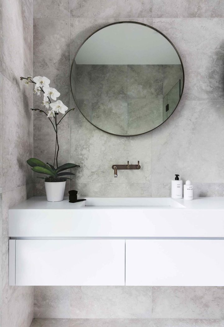 Hình ảnh một góc phòng tắm với chậu hoa lan nhỏ đặt cạnh gương soi, nổi bật trên nền tường bê tông xám