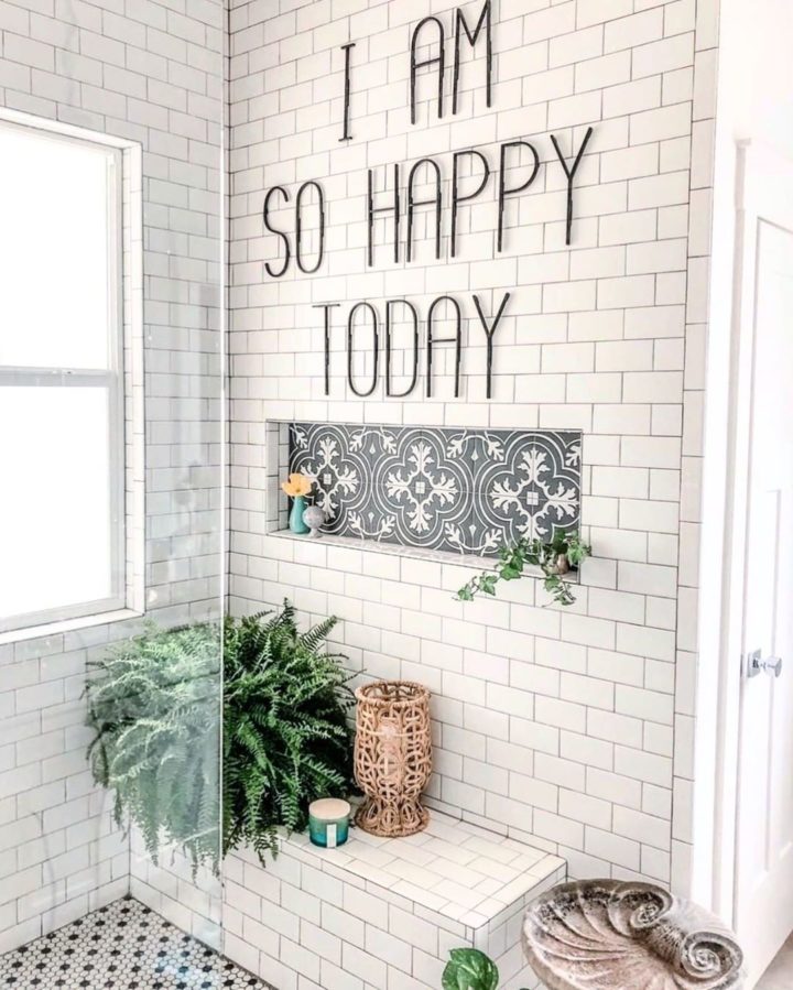 Hình ảnh cận cảnh một góc phòng tắm với tường ốp gạch me trắng, cửa sổ kính, dưới đặt chậu cây dương xỉ xanh tốt