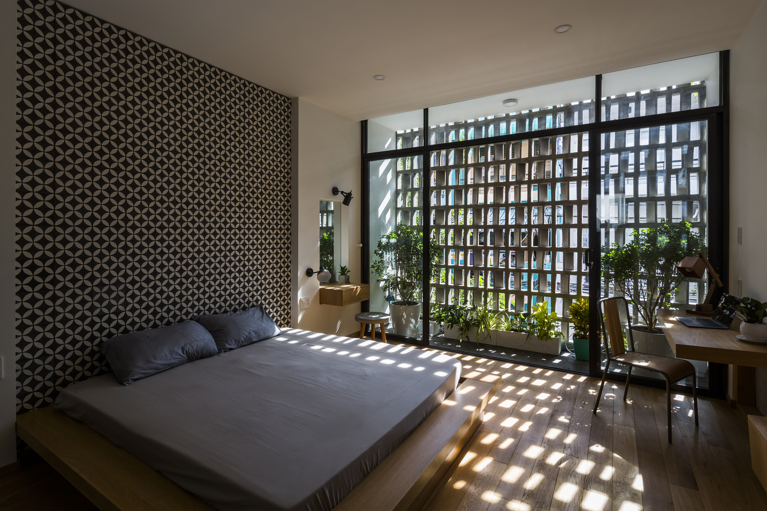 Hình ảnh phòng ngủ phong cách thiền tịnh với giường gỗ đặt sát nền, tường gạch bông, cửa kính trong suốt, trang trí cây xanh