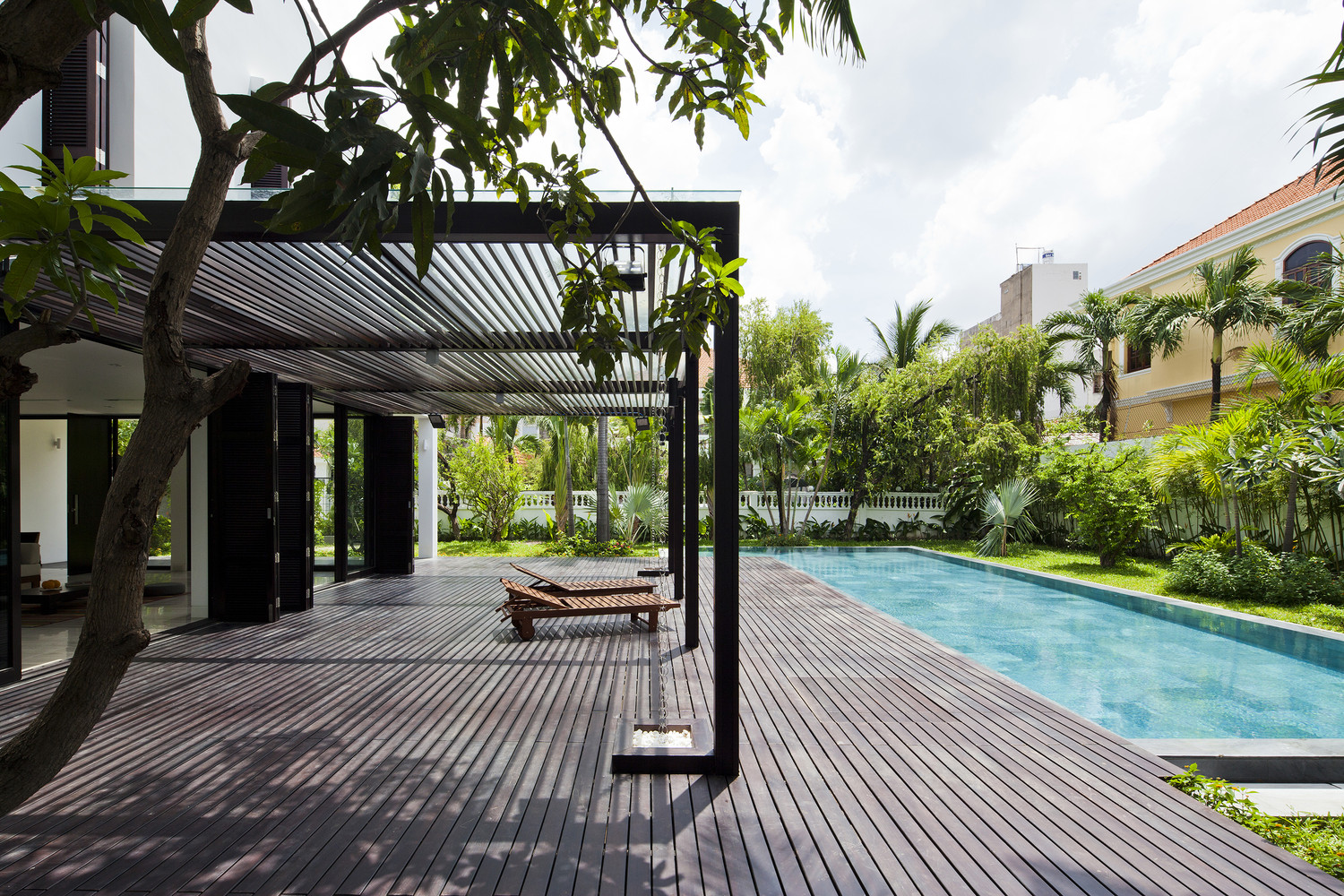 Kiến trúc sư thiết kế bể bơi như một phần mở rộng, kéo dài từ không sinh hoạt bên trong biệt thự. Hiên nhà lát gỗ có mái che là nơi thư giãn, tắm nắng lý tưởng.