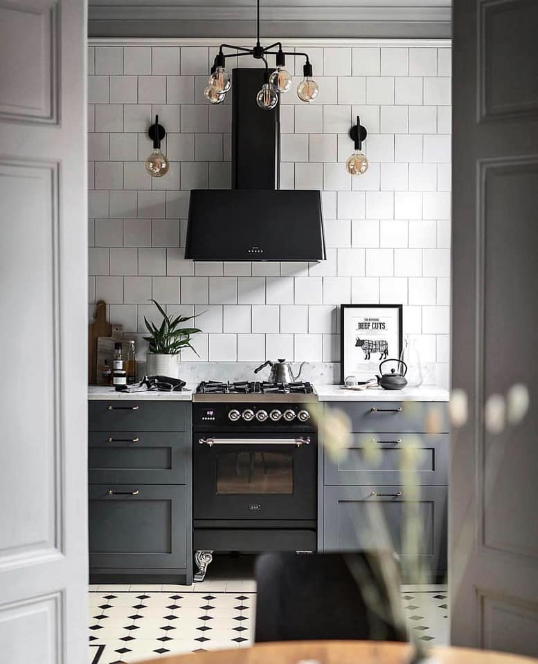 Hình ảnh một góc phòng bếp với tường ốp gạch màu trắng, máy hút mùi màu đen, đèn sợi đốt ấm áp