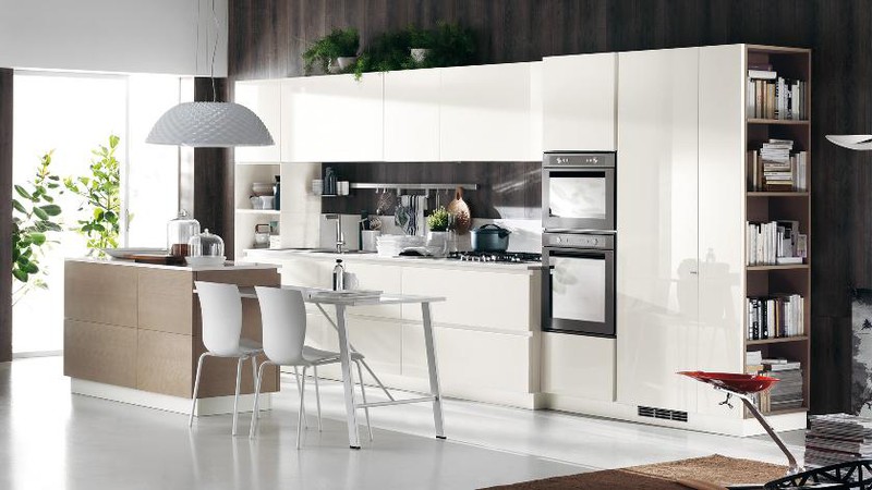 Hình ảnh phòng bếp với hệ tủ màu trắng cánh phẳng, bàn ăn kéo dài từ đảo bếp, cửa kính mở ra bên ngoài