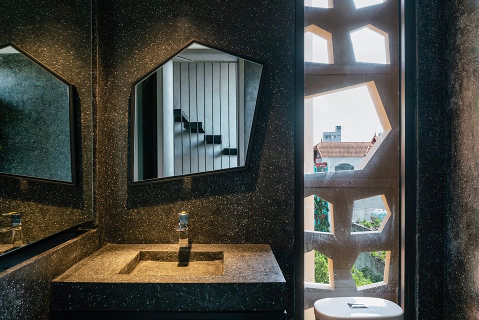 Hình ảnh cận cảnh một góc phòng vệ sinh với tường màu xám đen, khung cửa hình học lấy sáng tự nhiên