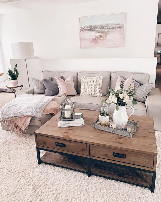 Hình ảnh một góc phòng khách màu be chủ đạo với sofa ghi xám, gối tựa màu hồng phấn, bàn trà gỗ, phía trên đặt bình cây xanh sinh động