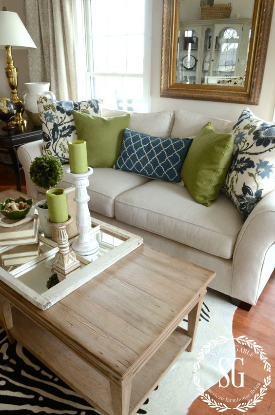 Hình ảnh một góc phòng khách màu be thoáng sáng với gối tựa họa tiết hoa lớn màu xanh nước biển đặt trên ghế sofa màu sữa, cửa sổ kính, đèn chụp chân đế mạ vàng