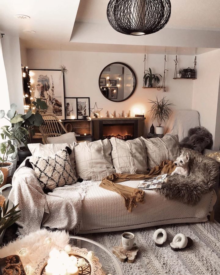 Hình ảnh một góc phòng khách màu be với sofa ghi lướn, chăn trải mềm mại, trang trí bằng khung gương tròn, đèn chùm độc đáo