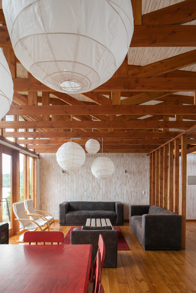 Hình ảnh phòng khách liên thông phòng ăn với dầm gỗ lớn, sàn nhà lát gỗ, bàn ghế hiện đại, trang trí bởi đèn thả trần màu trắng 