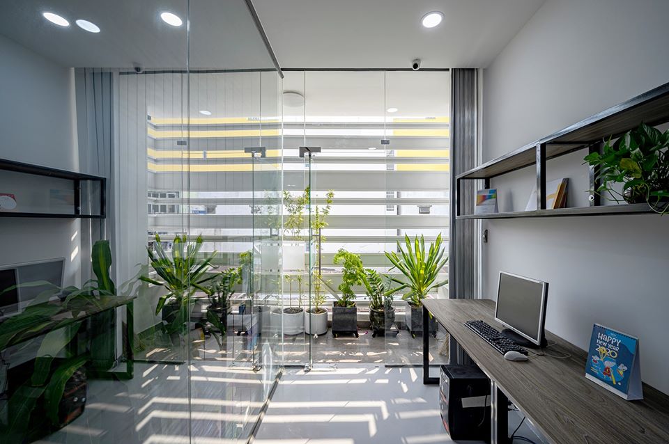 Hình ảnh cận cảnh một góc văn phòng với bàn ghế nhỏ gọn, cửa kính lớn, nhiều chậu cây xanh