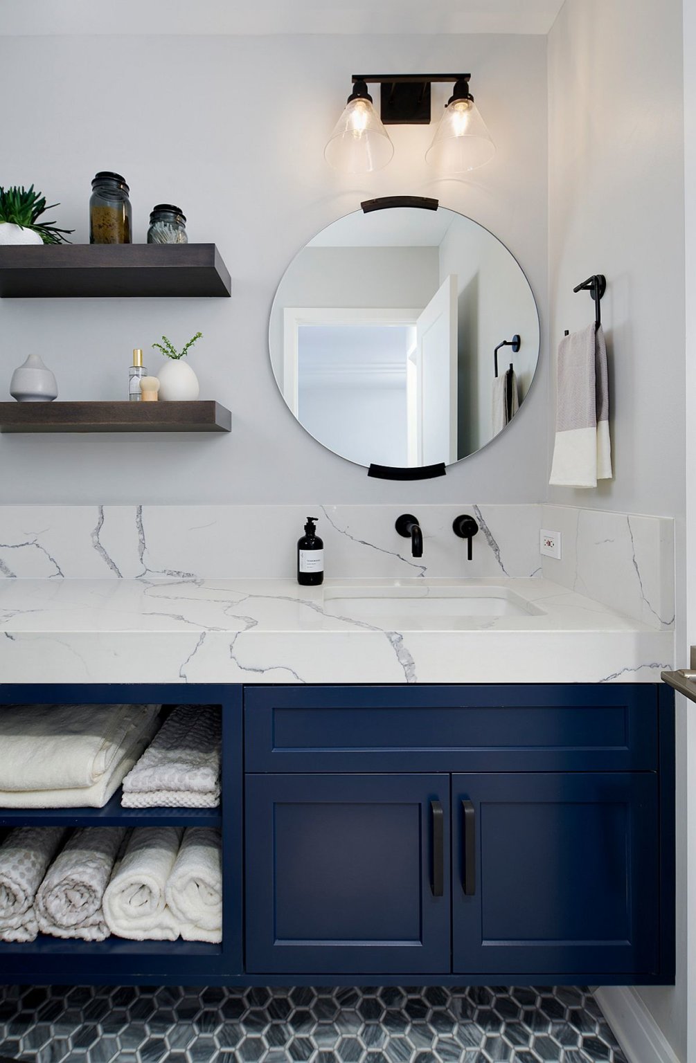 Hình ảnh một góc phòng tắm với nền tường màu trắng, gương tròn, tủ màu xanh dương đậm