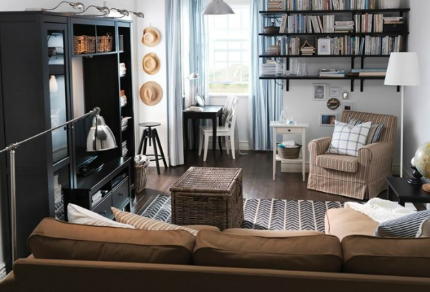 Hình ảnh một phòng khách nhỏ nhưng đầy đủ tiện nghi với tủ màu đen, sofa màu be, bàn trà và ghế tựa mây tre đan, cửa sổ kính, kệ mở gắn tường.
