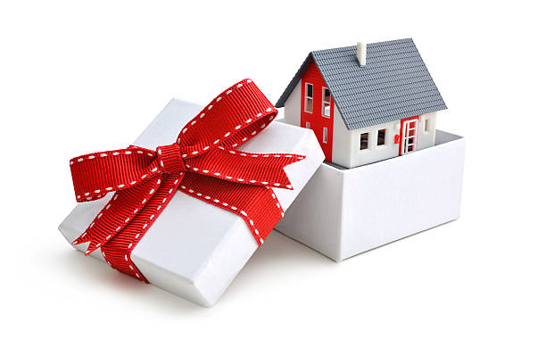 Hình ảnh cận cảnh một mô hình ngôi nhà được gói trong hộp quà buộc nơ màu đỏ đã mở nắp hộp.