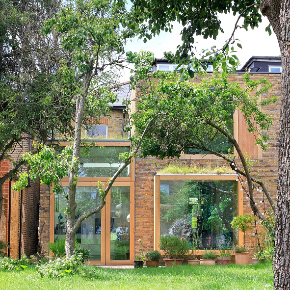 Hình ảnh toàn cảnh ngôi nhà phía Tây London sau cải tạo với vật liệu gạch, kính chủ đạo, cây xanh và thảm cỏ bao quanh