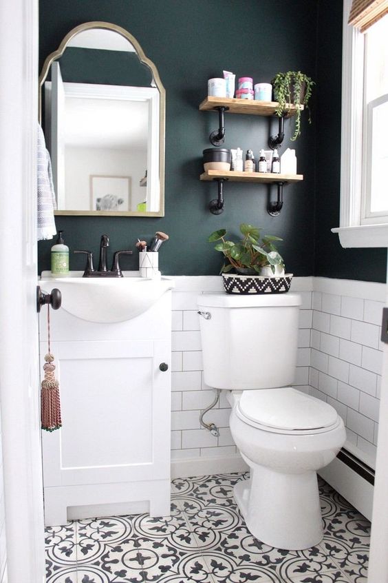 Hình ảnh bên trong phòng tắm nhỏ với mảng tường sơn màu xanh dương đậm, gương viền cổ điển, kệ mở gắn tường.