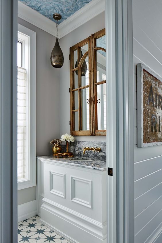 Hình ảnh một góc phòng tắm nhỏ với tường màu trắng, trần sơn xanh lam, đen trần ấn tượng, phía trên bồn rửa mặt là tủ gương khung gỗ mộc mạc.