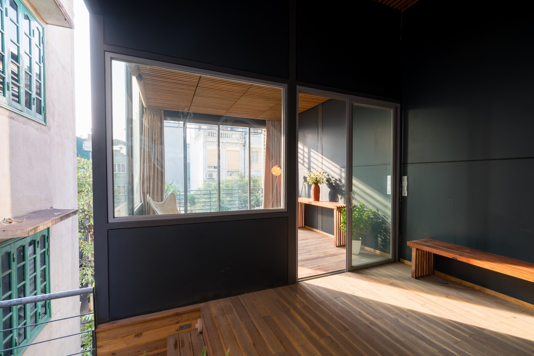Hình ảnh một góc trong căn hộ khung thép với ghế gỗ, tường sơn xanh dương đậm, cửa kính trong suốt