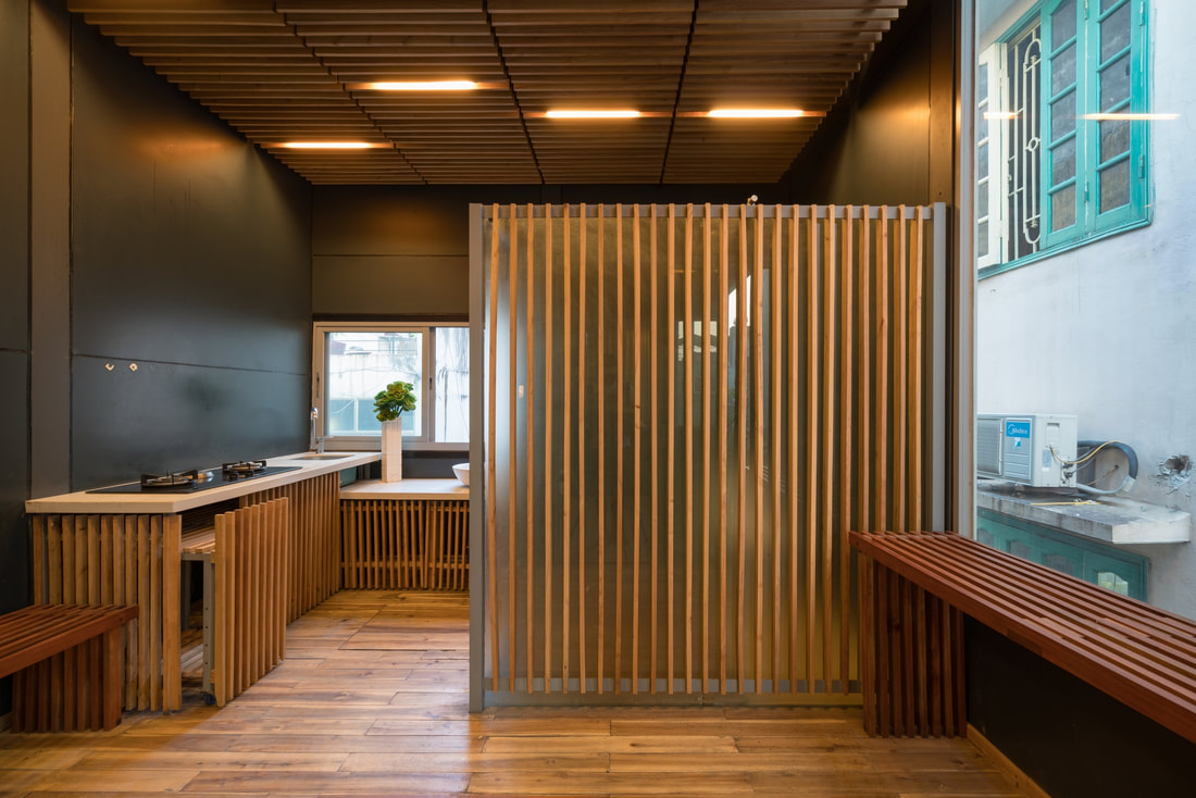 Hình ảnh toàn cảnh phòng bếp nhìn từ ngoài vào với lam gỗ cùng tông với hệ tủ bếp, trần và sàn nhà.