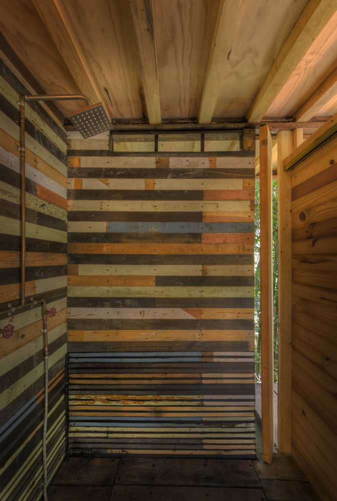 Hình ảnh phòng tắm trong ngôi nhà gỗ với vòi sen lớn bằng đồng, tường gỗ sơn kẻ ngang màu sắc tươi sáng.
