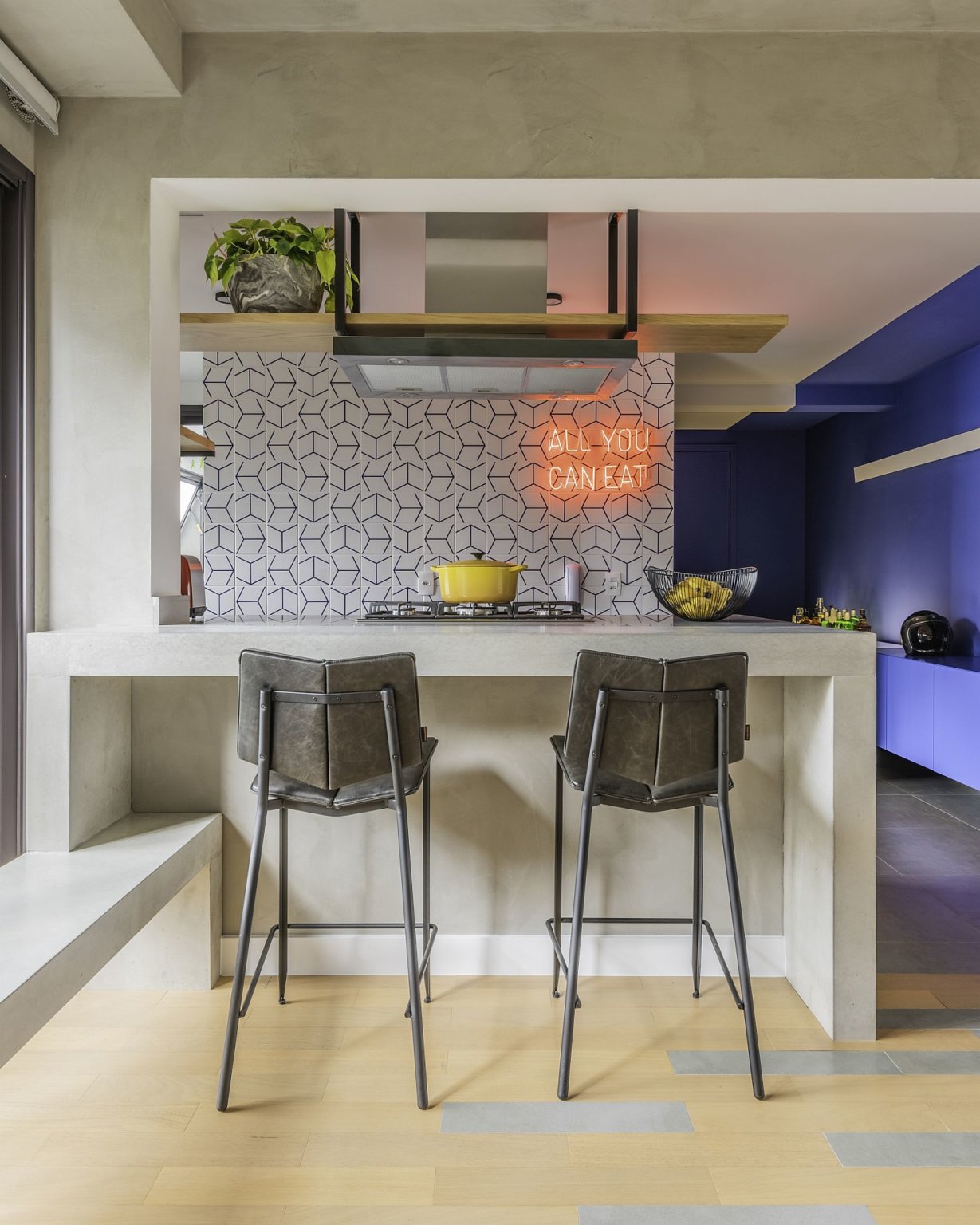 Hình ảnh toàn cảnh đảo bếp trong căn hộ đương đại với 2 ghế bar màu xám, tường ốp gạch men, kệ treo trần nhà.