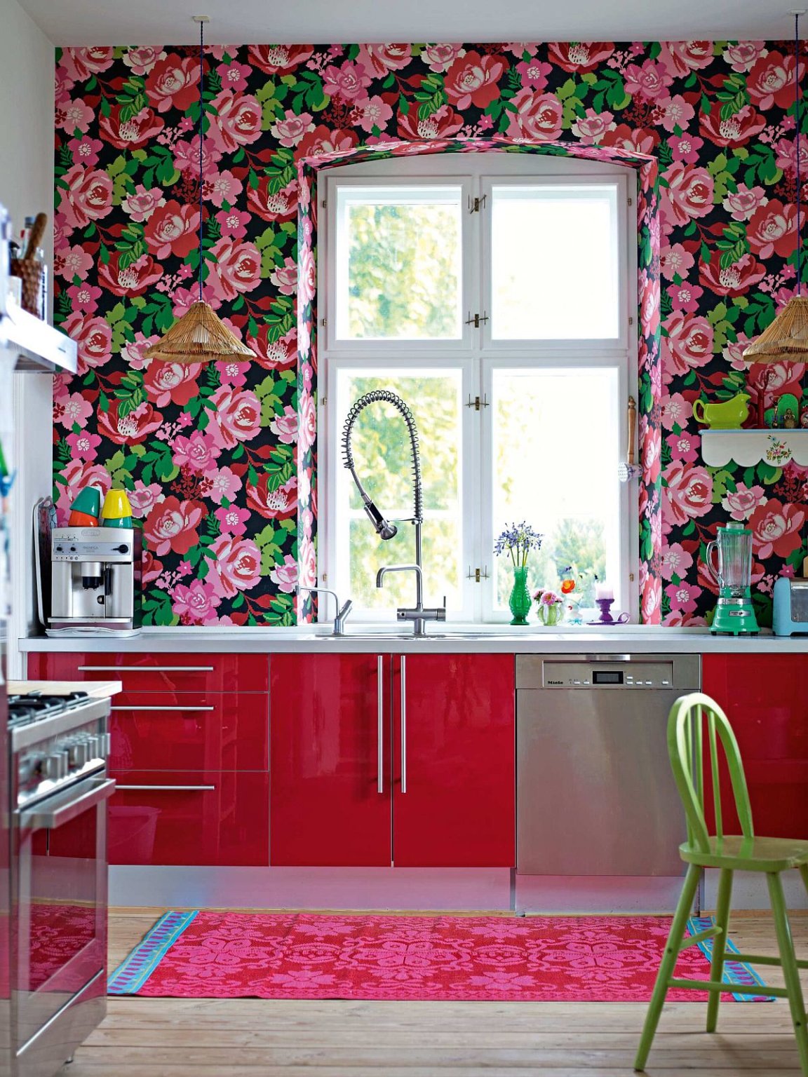 Hình ảnh một góc phòng bếp cực ấn tượng với giấy dán tường họa tiết hoa hồng lớn bao quanh khung cửa sổ, tủ bếp màu đỏ cùng tông với thảm chùi chân