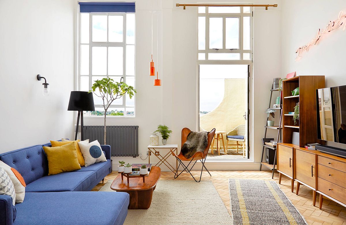 Hình ảnh toàn cảnh phòng khách nhỏ với sofa màu xanh lam, bàn trà gỗ, đối diện là tủ kệ tivi có ngăn kéo, cửa sổ kính trong suốt