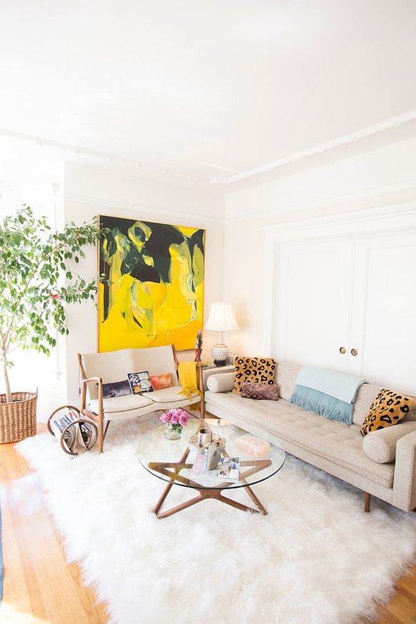 Hình ảnh phòng khách nhỏ ấn tượng với sofa trắng sữa, bàn trà kính, tranh treo tường màu vàng cam nổi bật