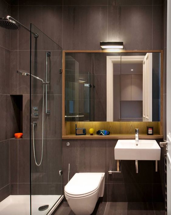 Hình ảnh phòng tắm với tường và sàn ốp lát gạch màu nâu đen, buồng tắm đứng vòi hoa sen tách biệt với khu vệ sinh bên ngoài bởi vách kính trong suốt trong nhà cấp 4 mái Thái