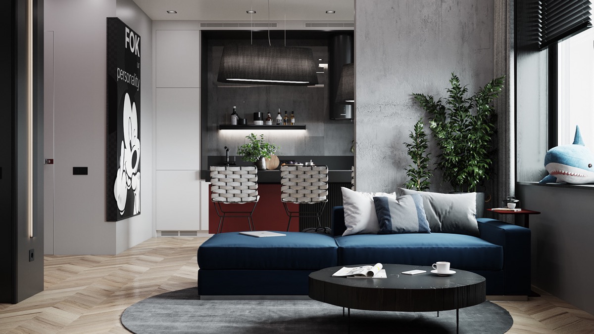 Hình ảnh toàn cảnh phòng khách căn hộ studio với ghế sofa màu xanh dương, bàn trà hình tròn màu đen lớn đặt trên thảm trải màu xám, góc phòng đặt chậu cây xanh lớn, cạnh đó là khu bếp nấu hiện đại