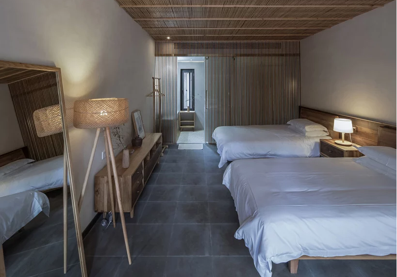 Hình ảnh toàn cảnh phòng ngủ giường đôi trong khách sạn gỗ, với trần, tủ kệ, đèn sàn đều làm từ chất liệu gỗ, tre mộc mạc.