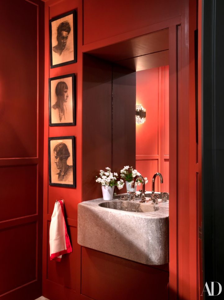 Hình ảnh phòng tắm màu đỏ với gương lớn gắn tường, bên cạnh treo ảnh đen trắng, bồn rửa bằng đá, lọ hoa trang trí