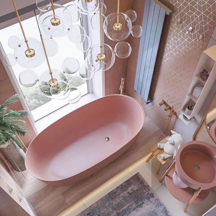 Hình ảnh phòng tắm tông màu hồng dịu ngọt với bồn tắm, chậu rửa đều màu hồng, đèn thả trang trí với phần thân mạ đồng