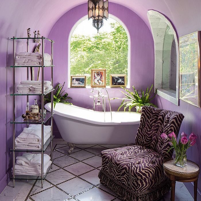 Hình ảnh phòng tắm màu tím với khung cửa vòm lớn mở ra sân vườn, bồn tắm đặt cạnh cửa sổ, giá kệ inox nhiều tầng ngay cạnh, ghế thư giãn bọc nệm họa tiết da báo.
