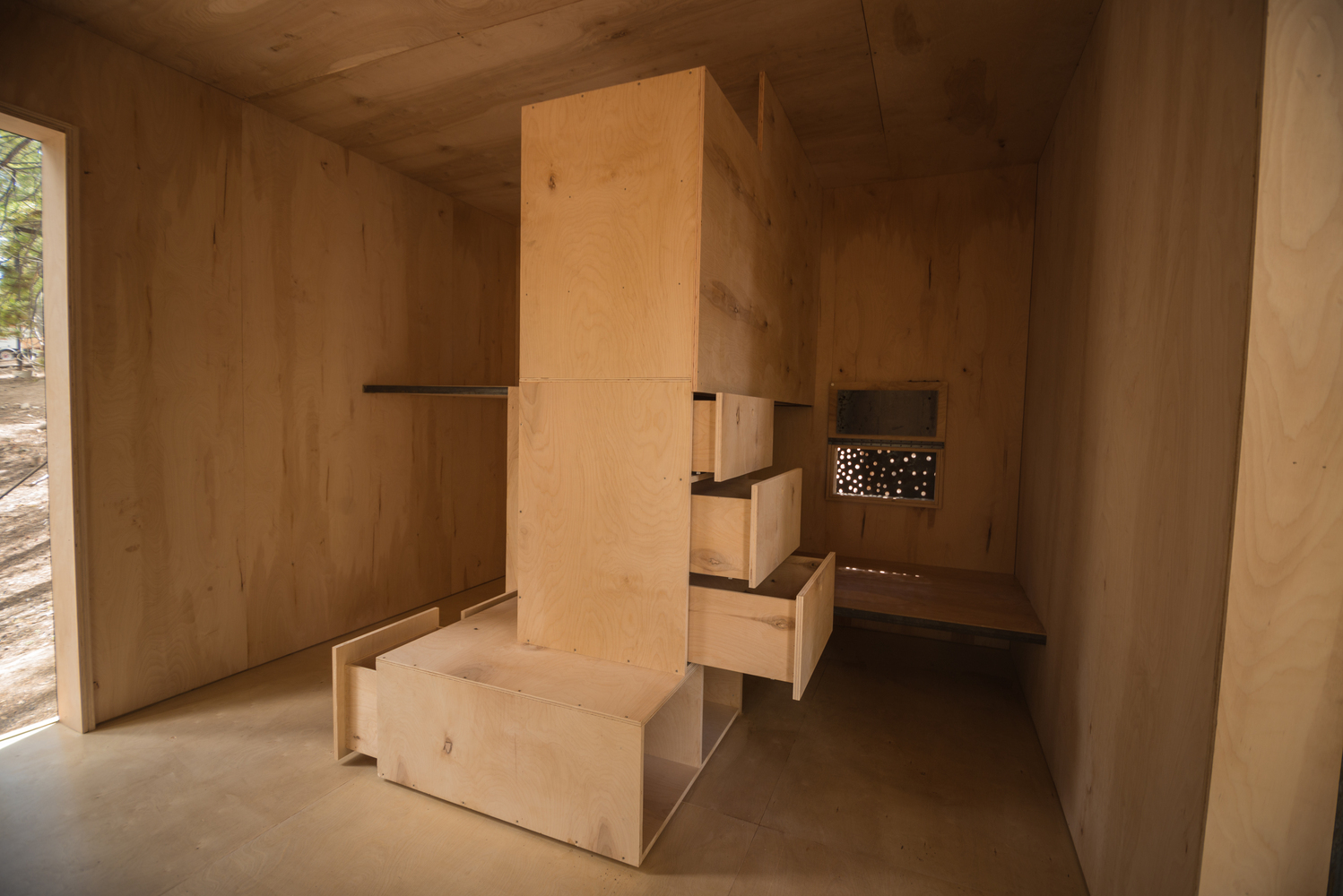 Hình ảnh một căn phòng nhỏ làm bằng gỗ chủ đạo, ở giữa đặt tủ kệ bằng gỗ có nhiều ngăn kéo.