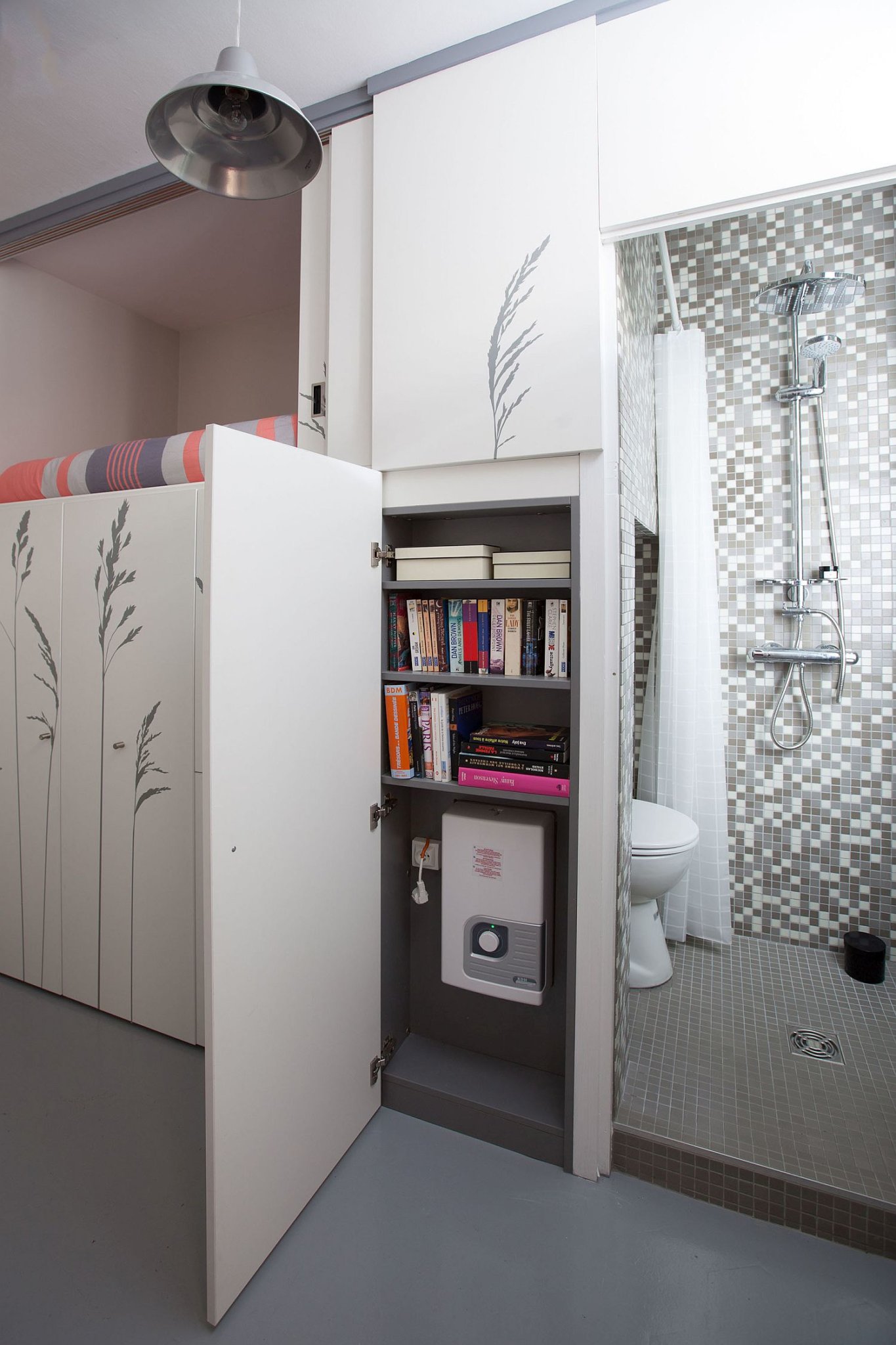 Hình ảnh phòng tắm căn hộ siêu nhỏ với tủ màu trắng phía ngoài đựng sách báo, hộp kỹ thuật