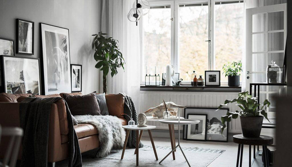 Hình ảnh phòng khách phong cách nội thất Japandi với điểm nhấn là bộ ghế sofa màu nâu da bò, tranh treo tường đen trắng, trang trí chậu cây xanh, lấy sáng tự khung cửa sổ kính trong suốt.