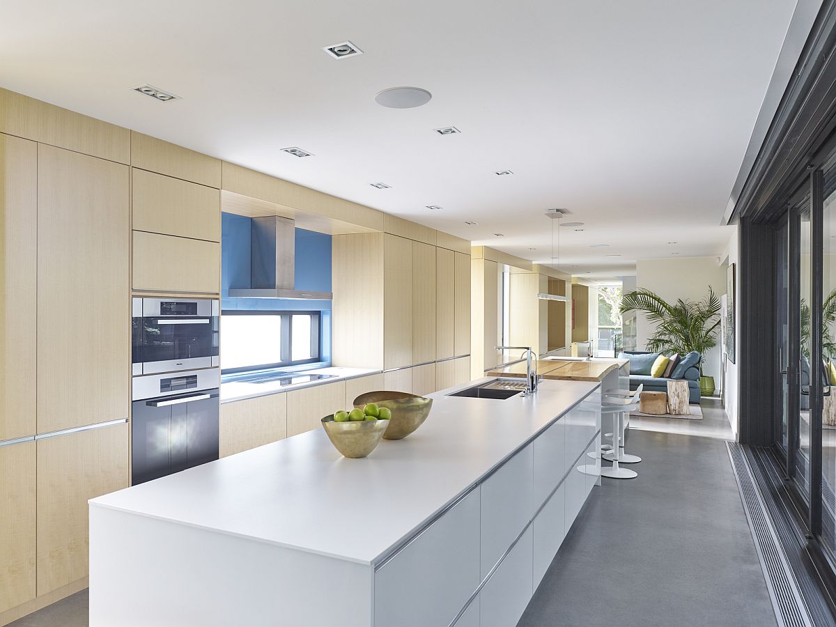 Hình ảnh toàn cảnh phòng bếp hiện đại với hệ tủ bếp bằng gỗ cao kịch trần, bàn bếp màu trắng đối diện