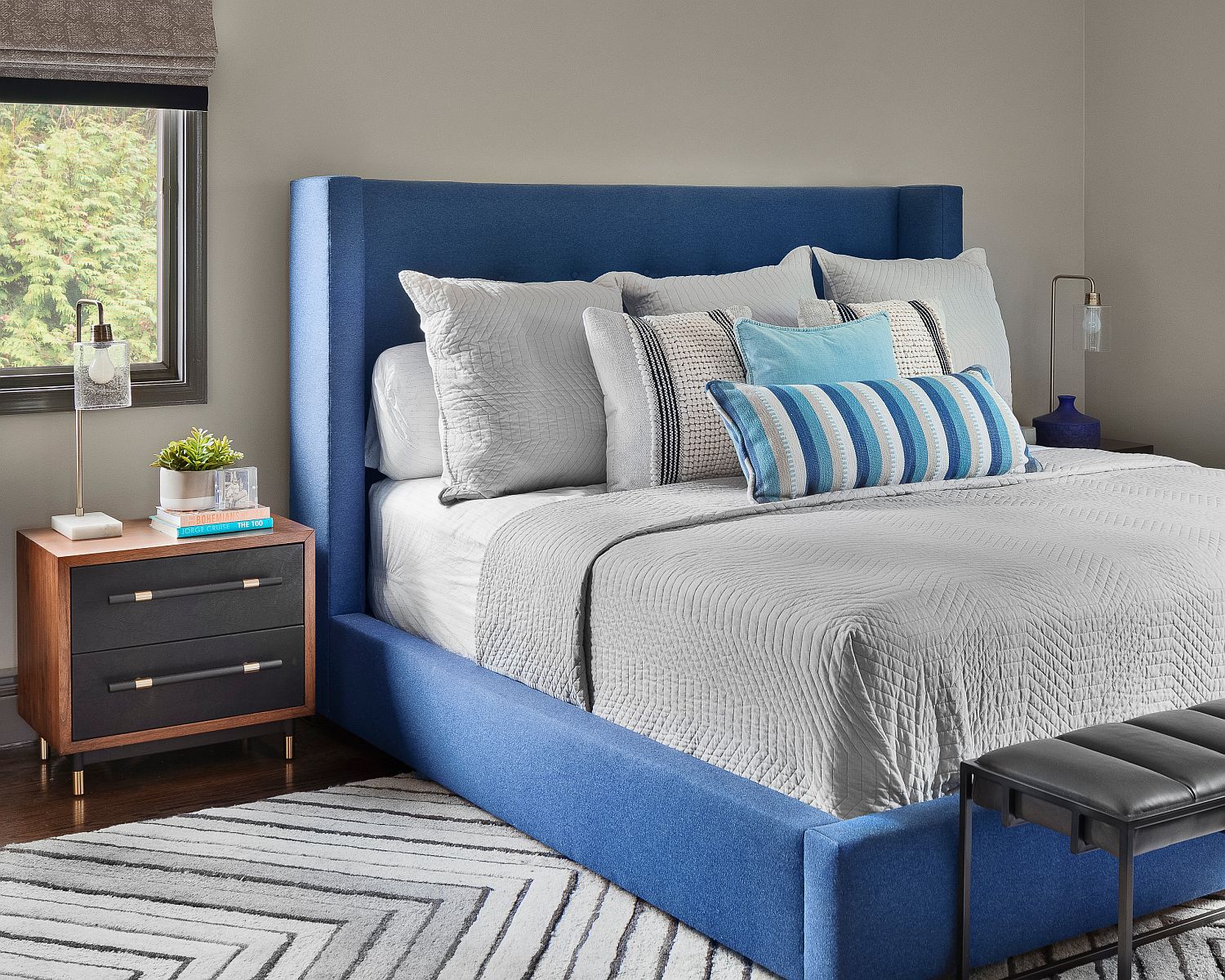 Hình ảnh phòng ngủ hiện đại với giường nệm màu xanh, tủ ngăn kéo đầu giường bằng gỗ, chân bọc đồng