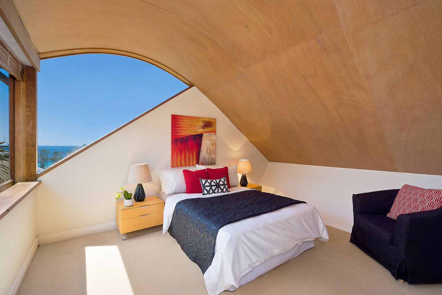 Hình ảnh phòng ngủ nhỏ trên tầng áp mái với trần gỗ cong mềm mại, giường nệm màu trắng, cửa sổ kính lớn