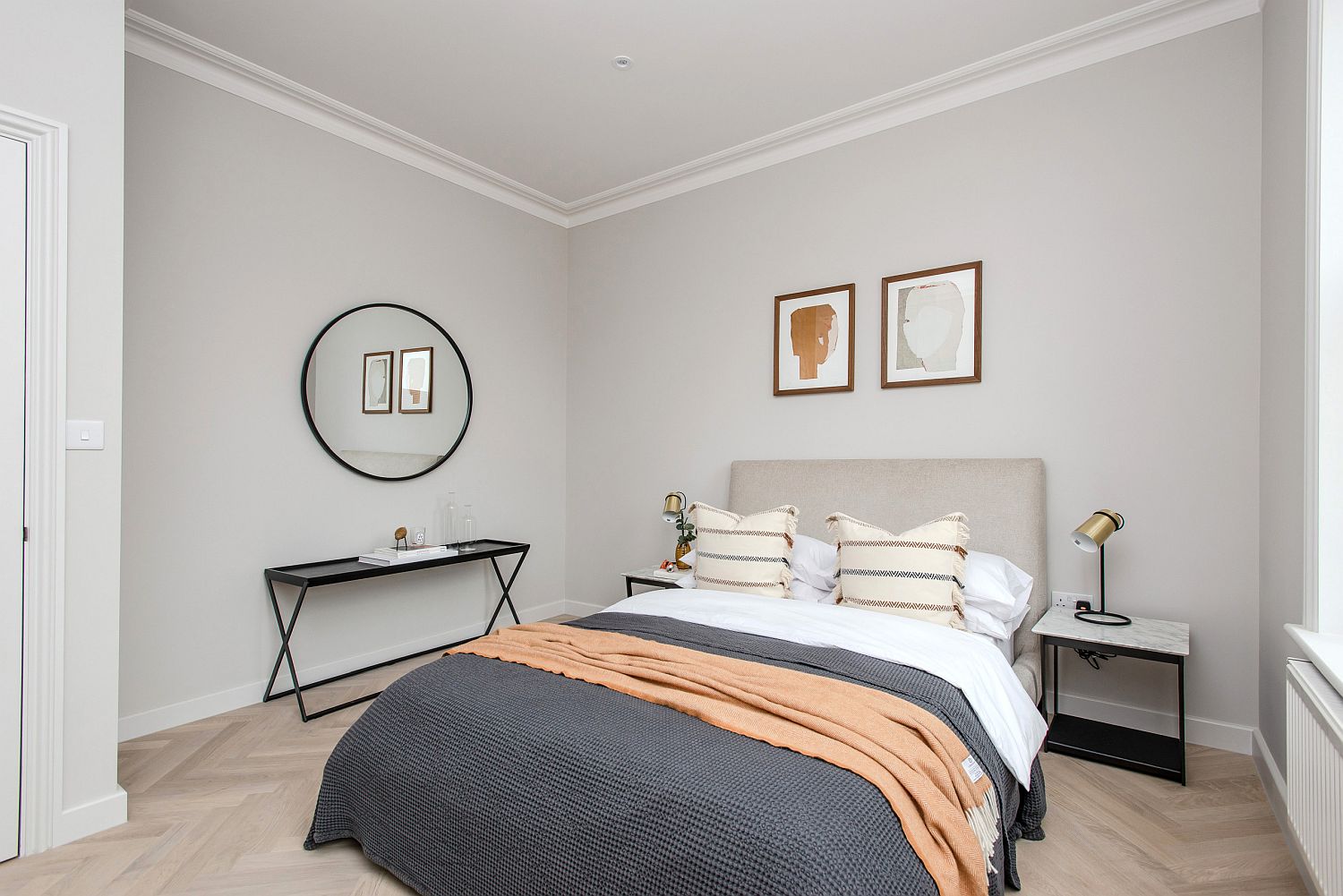 Hình ảnh phòng ngủ gam màu xám trắng chủ đạo với hai tranh treo đầu giường, gương tròn và kệ màu đen ấn tượng
